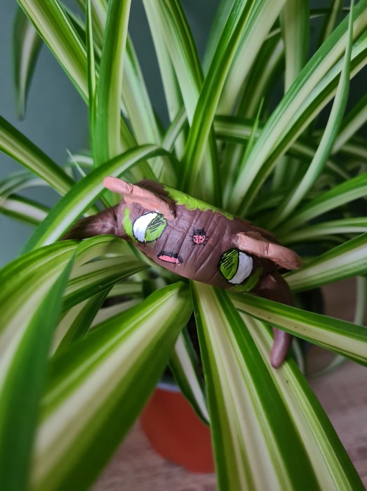 a painted clay sculpture of a tree stump character. Photographed sitting in a potted plant