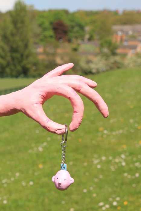 A keyring of a man's head. Displayed on a pink hand sculpture