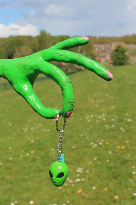 A keyring of an alien's head. Displayed on a green alien hand sculpture