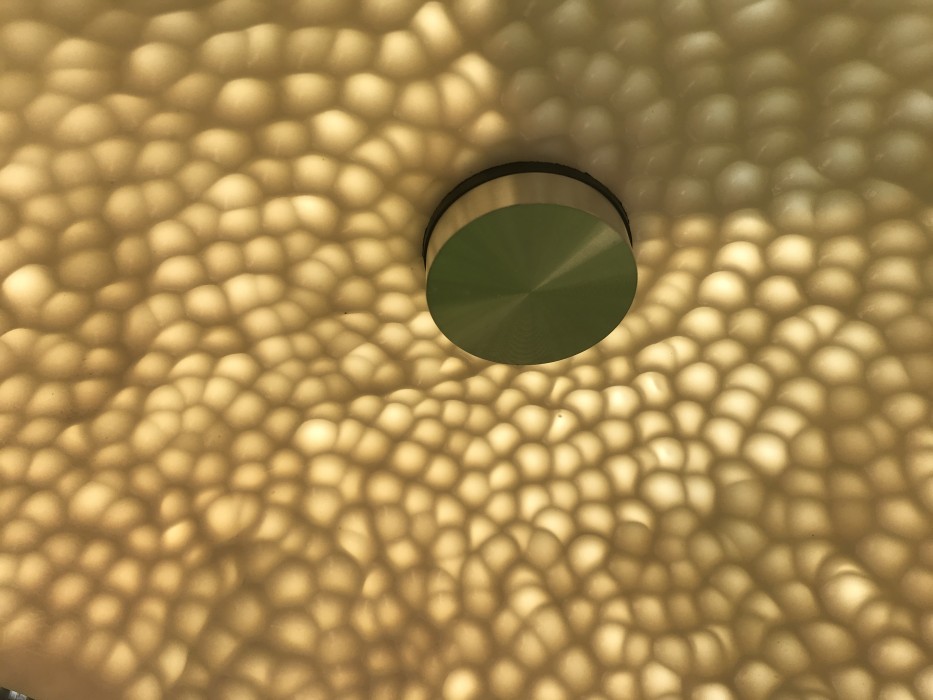 Close detail of the underside of a single porcelain lobe, showing it glowing with natural sun light. Shows aluminium fixture detail which holds the lobe in place.